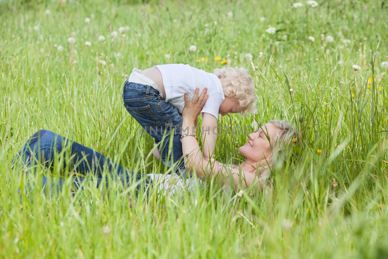 Mother lying on grass and playing with son by leaf