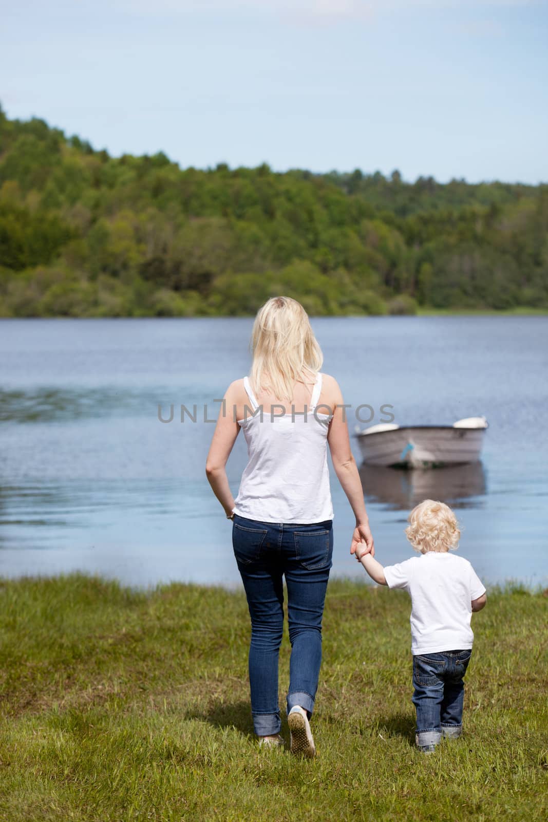 A mother walking with her son hear a lake with a small boat