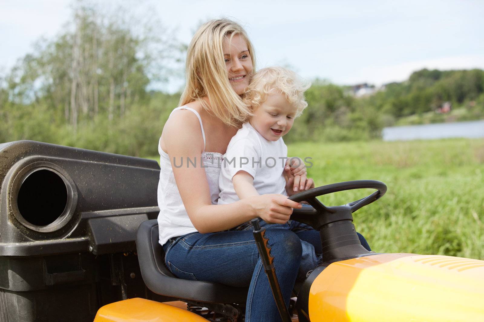 Smiling young woman with adorable child sitting on lawn mower