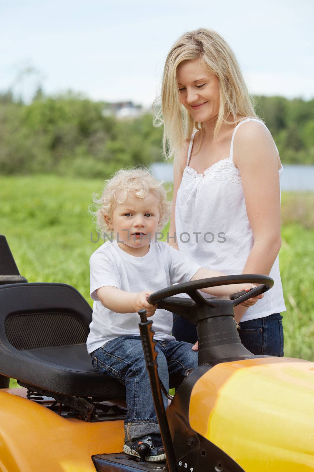 Smiling mother standing near baby boy holding steering wheel