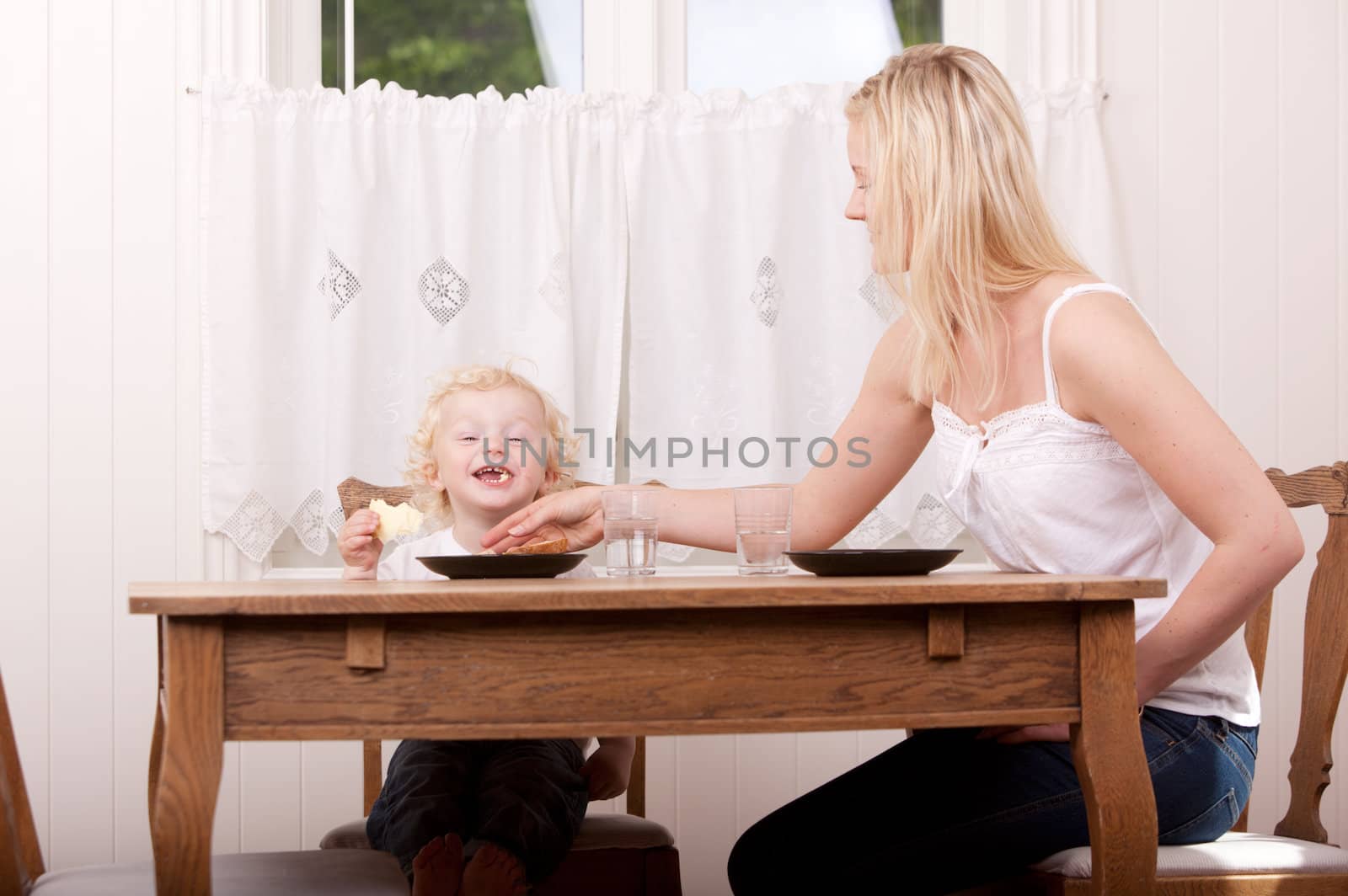 A happy boy smiling with excitement at the camera, sitting at meal table with mother