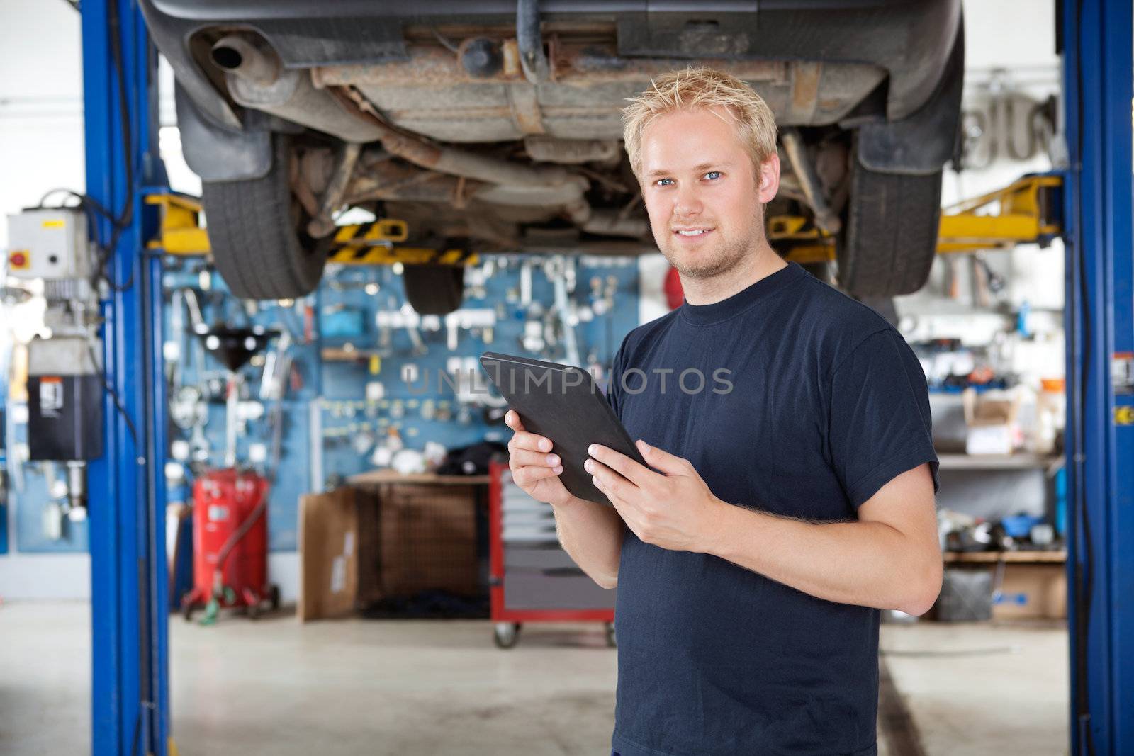 Portrait of young mechanic holding digital tablet in his auto repair shop