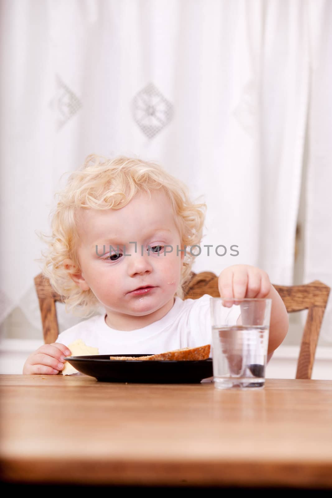 A young child sitting a a table reaching for glass of water