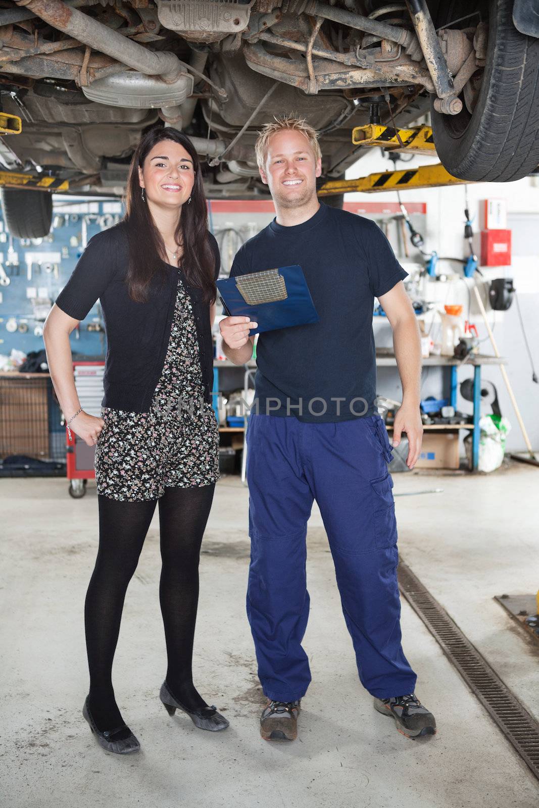 Portrait of young mechanic standing with female customer in auto repair shop