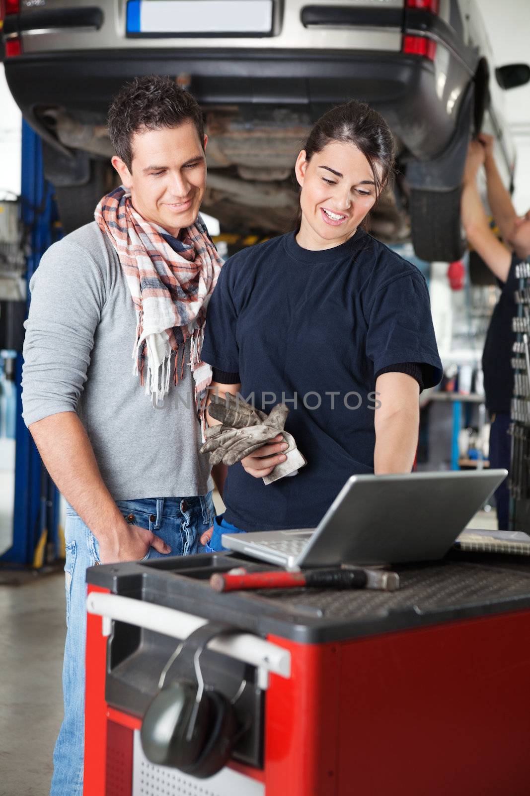 Female mechanic using laptop with client by leaf