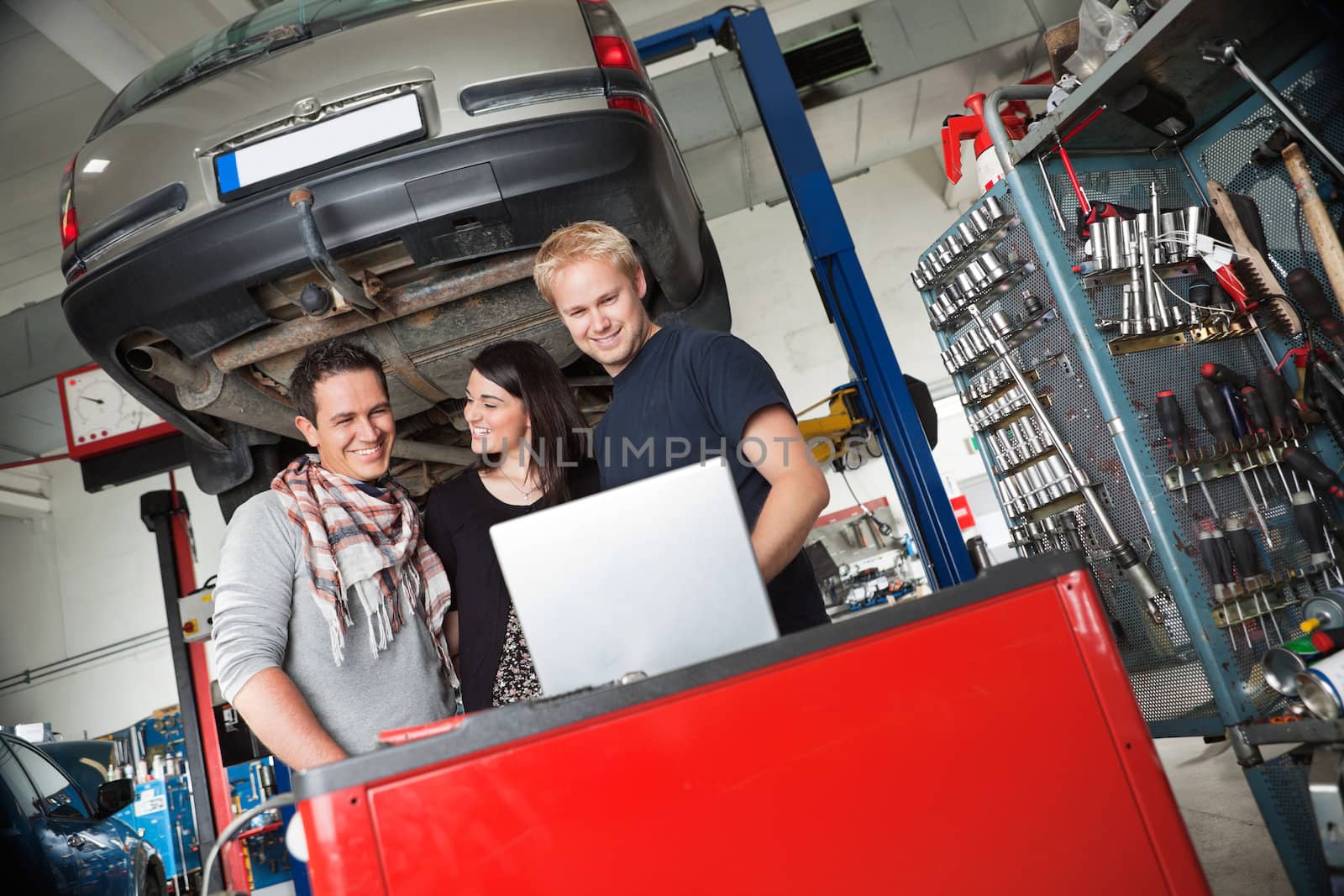 Couple in auto repair shop standing with mechanic by leaf