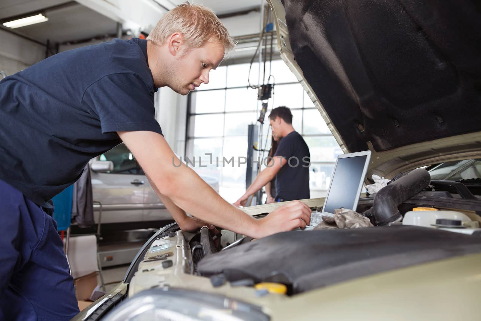 Mechanic using laptop while working on car with people in background