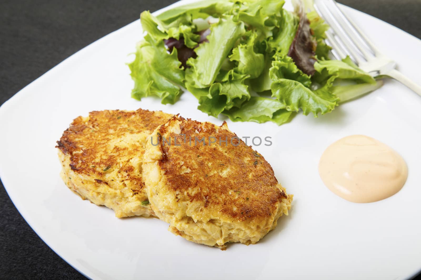 Fresh crab cakes on a white plate with sauce and a salad of field greens