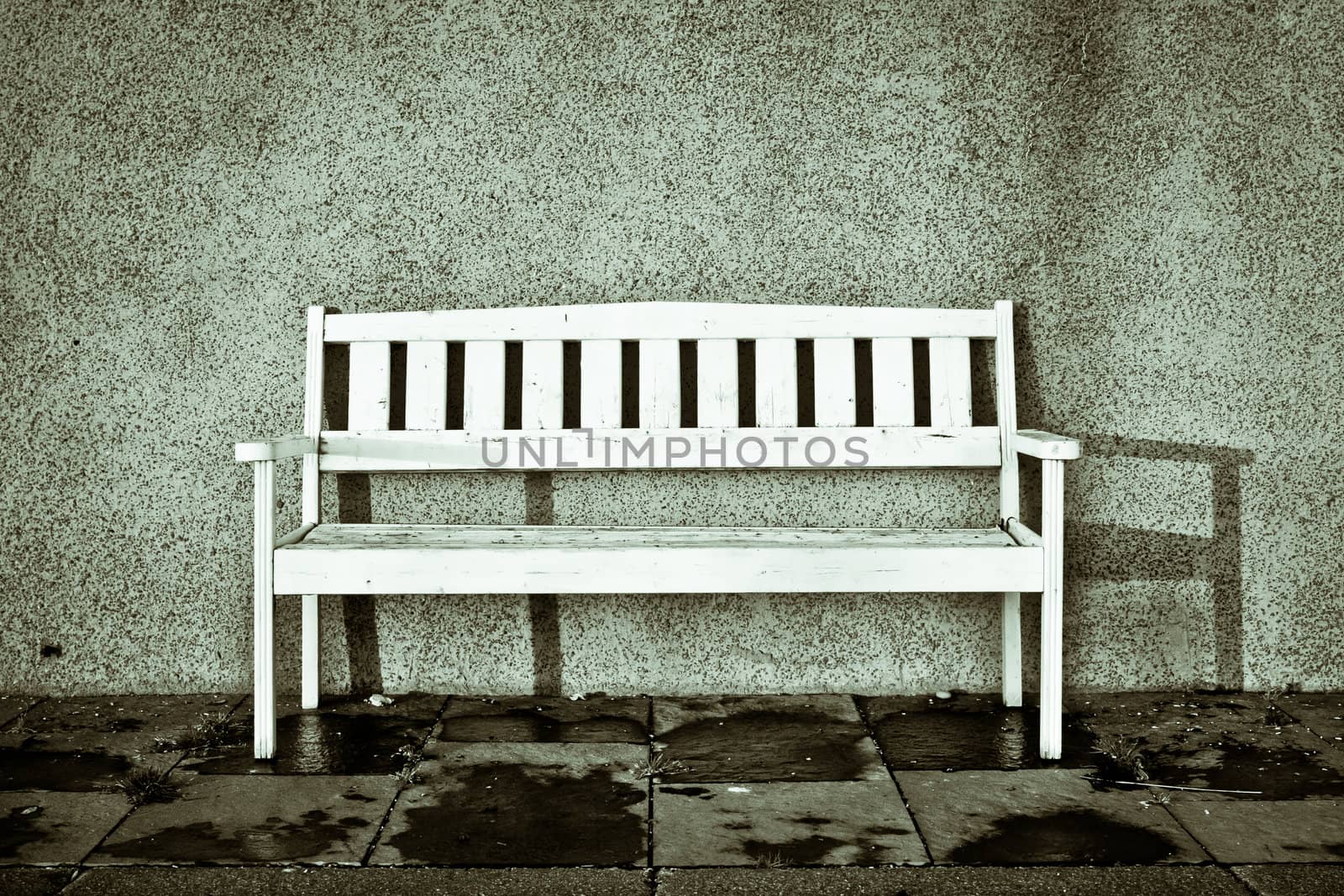 A white bench on a town street with shadow from sunlight