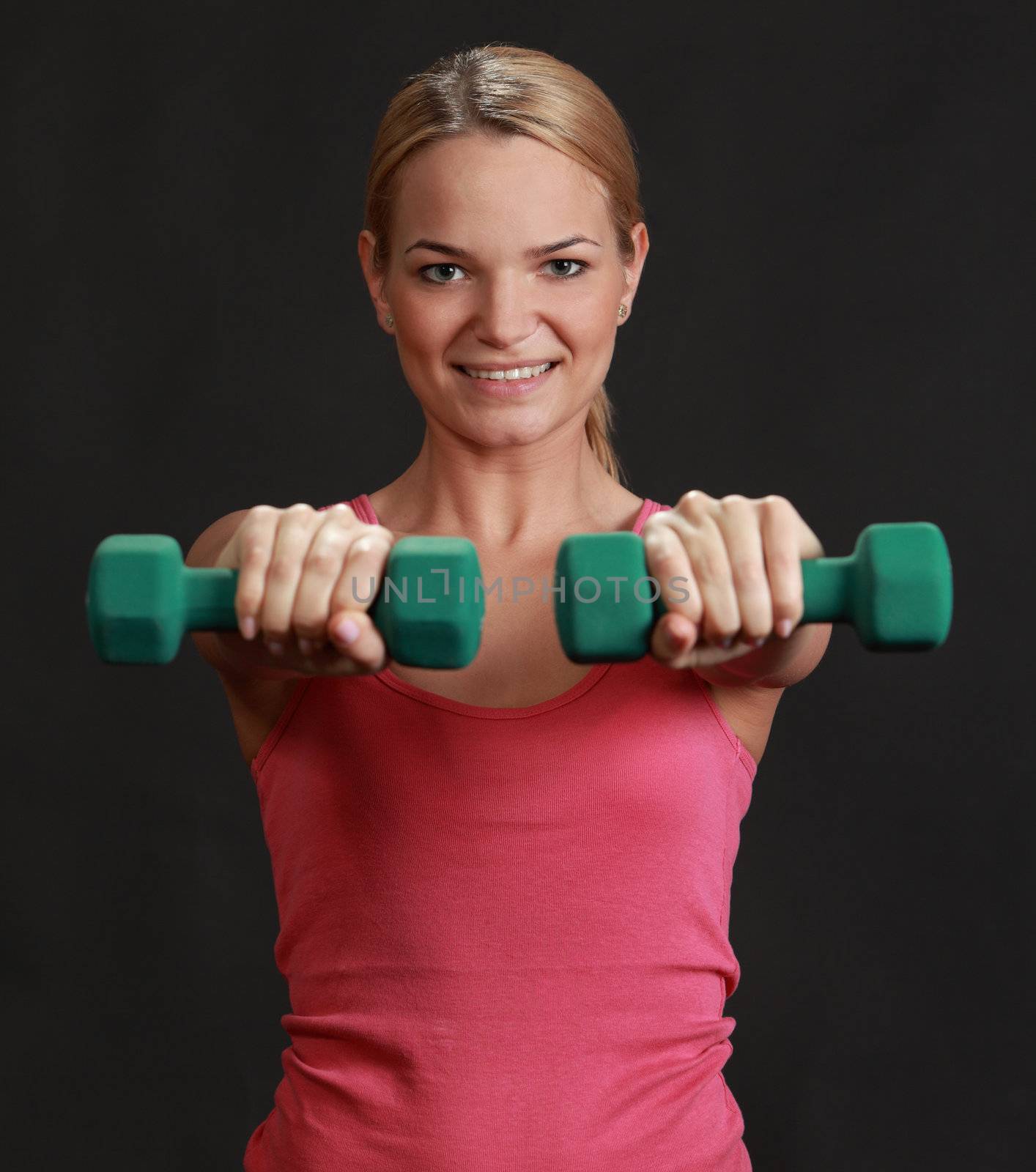 Portrait of a young blonde woman doing exercise with dumbbellsagainst a black background.