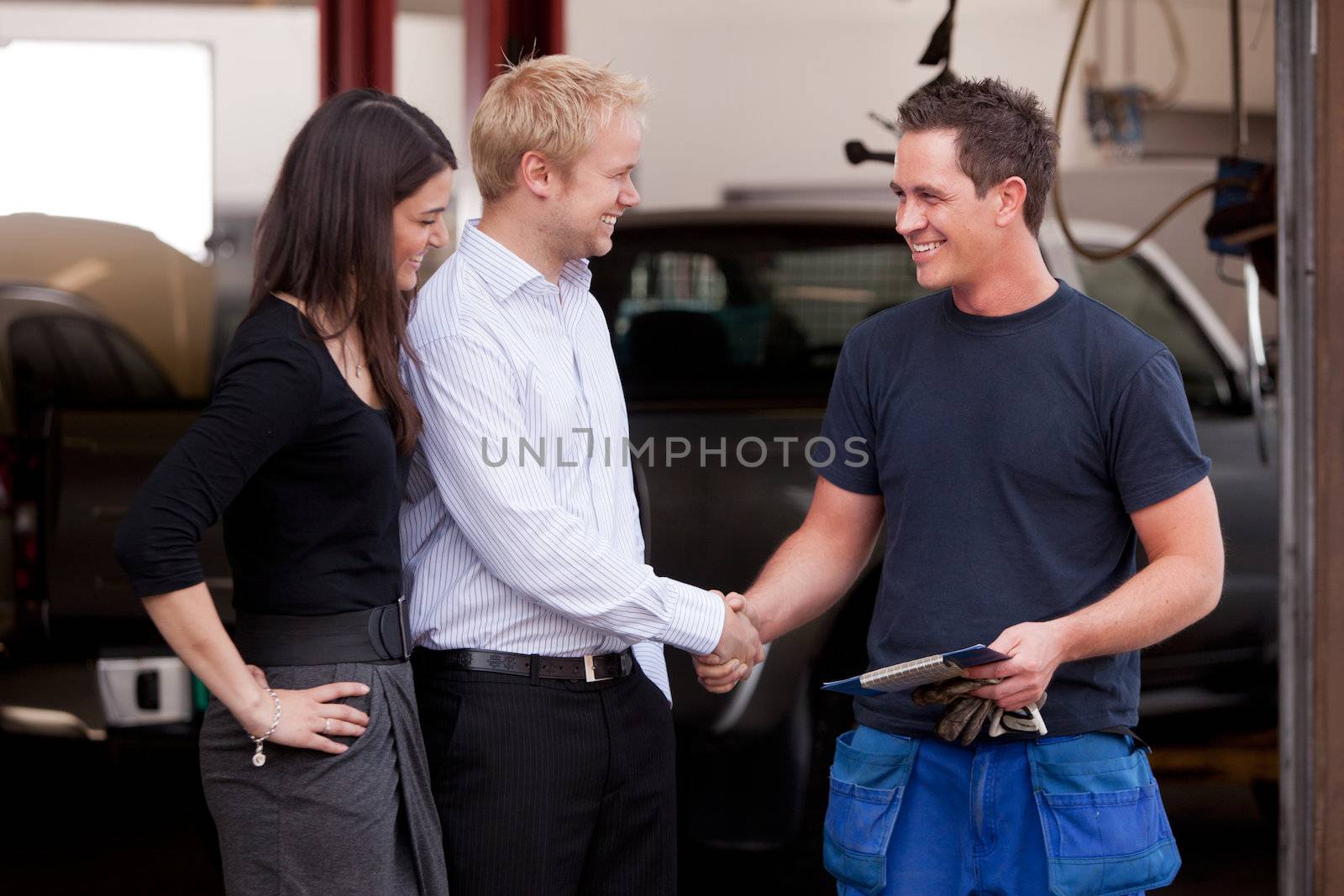 A happy attractive mechanic shaking hands with a customer couple,happy with their service