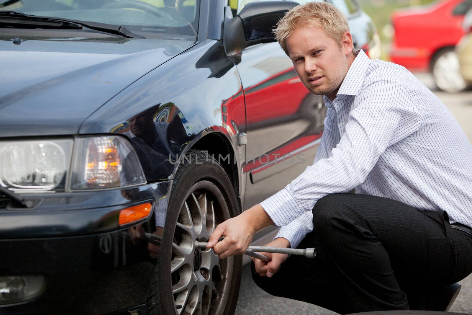 An unhappy business man changing a tire on the road