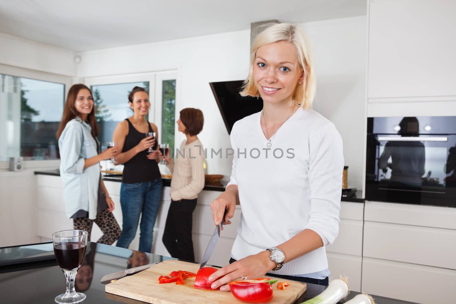 Portrait of happy female cutting vegetables while friends having drink in background