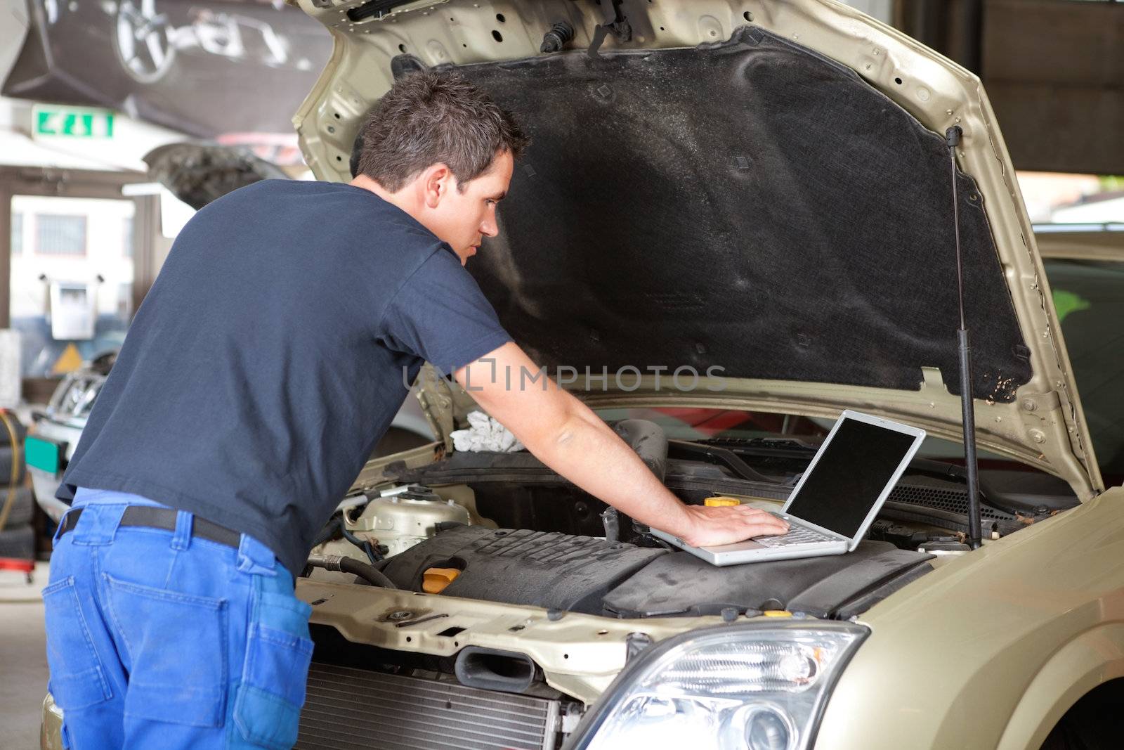 Mechanic using laptop while repairing car in garage