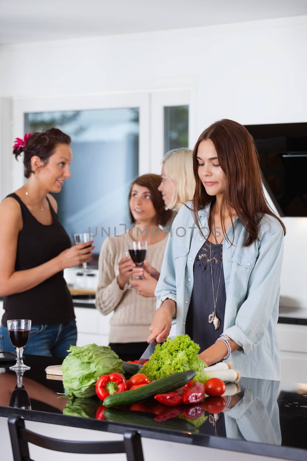 Pretty female cutting vegetables while her friends having drink in background