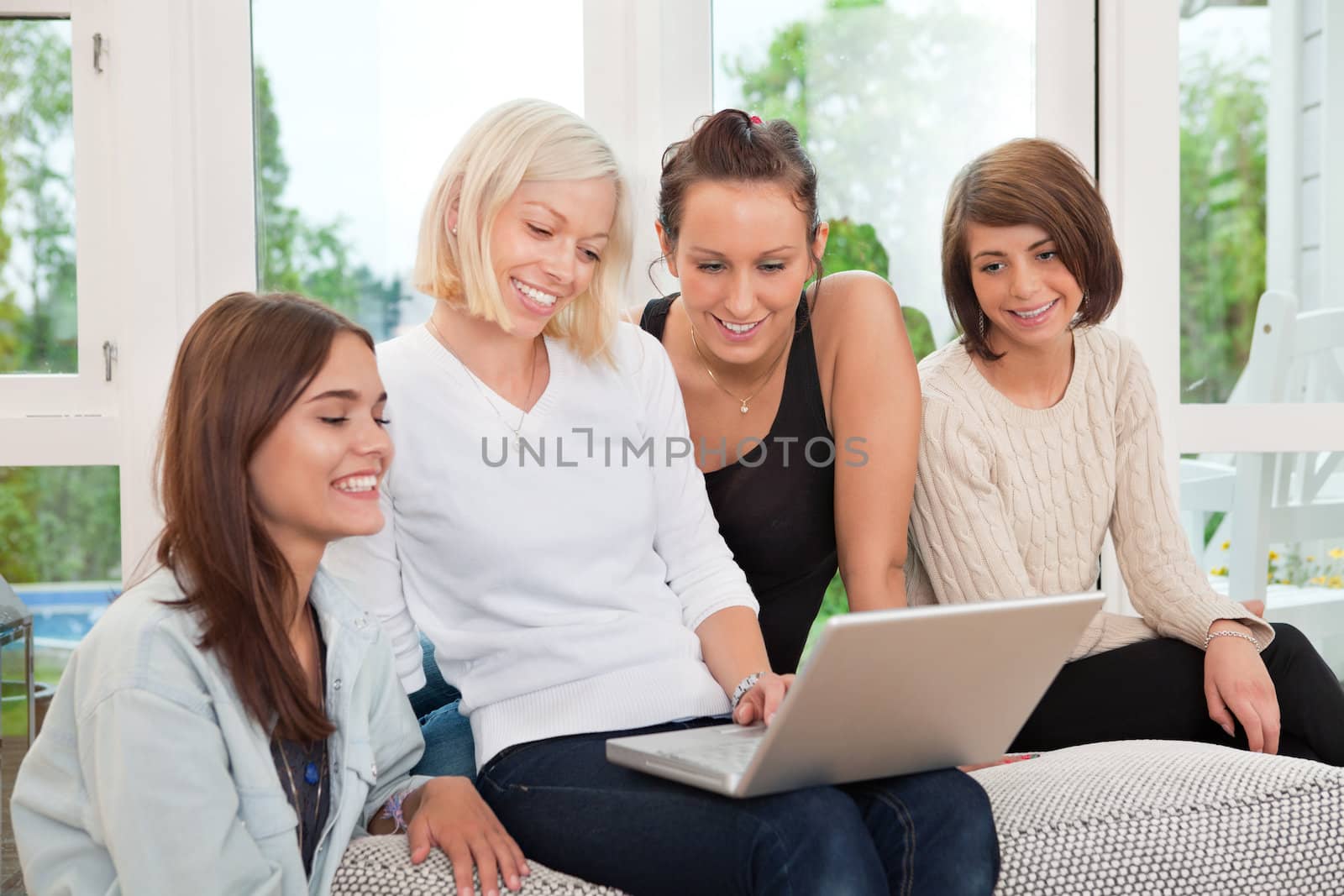 Group of smiling female friends sitting on couch and looking at laptop
