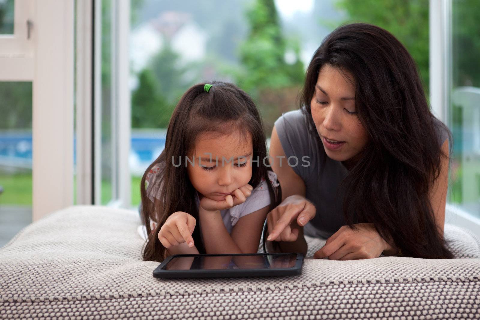 Mother and daughter laying on couch playing with a digital tablet