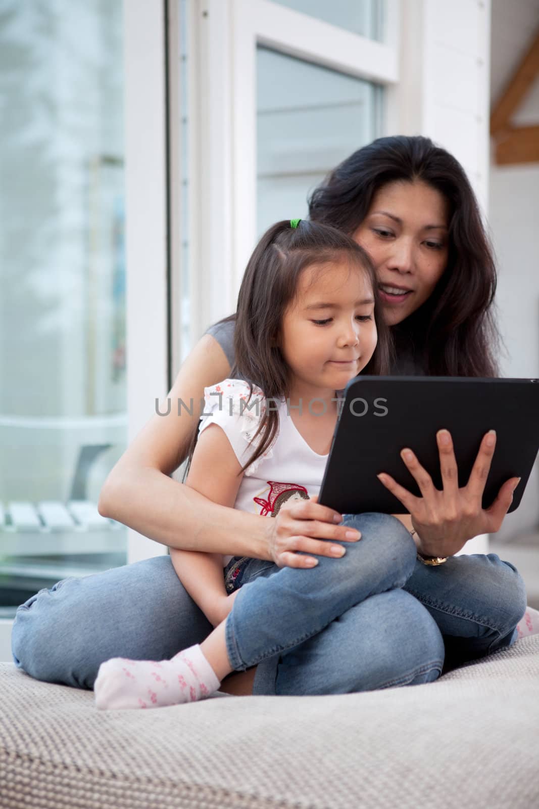 Happy mother and daughter using a digital tablet in a home interior, shallow depth of field with critical focus on child