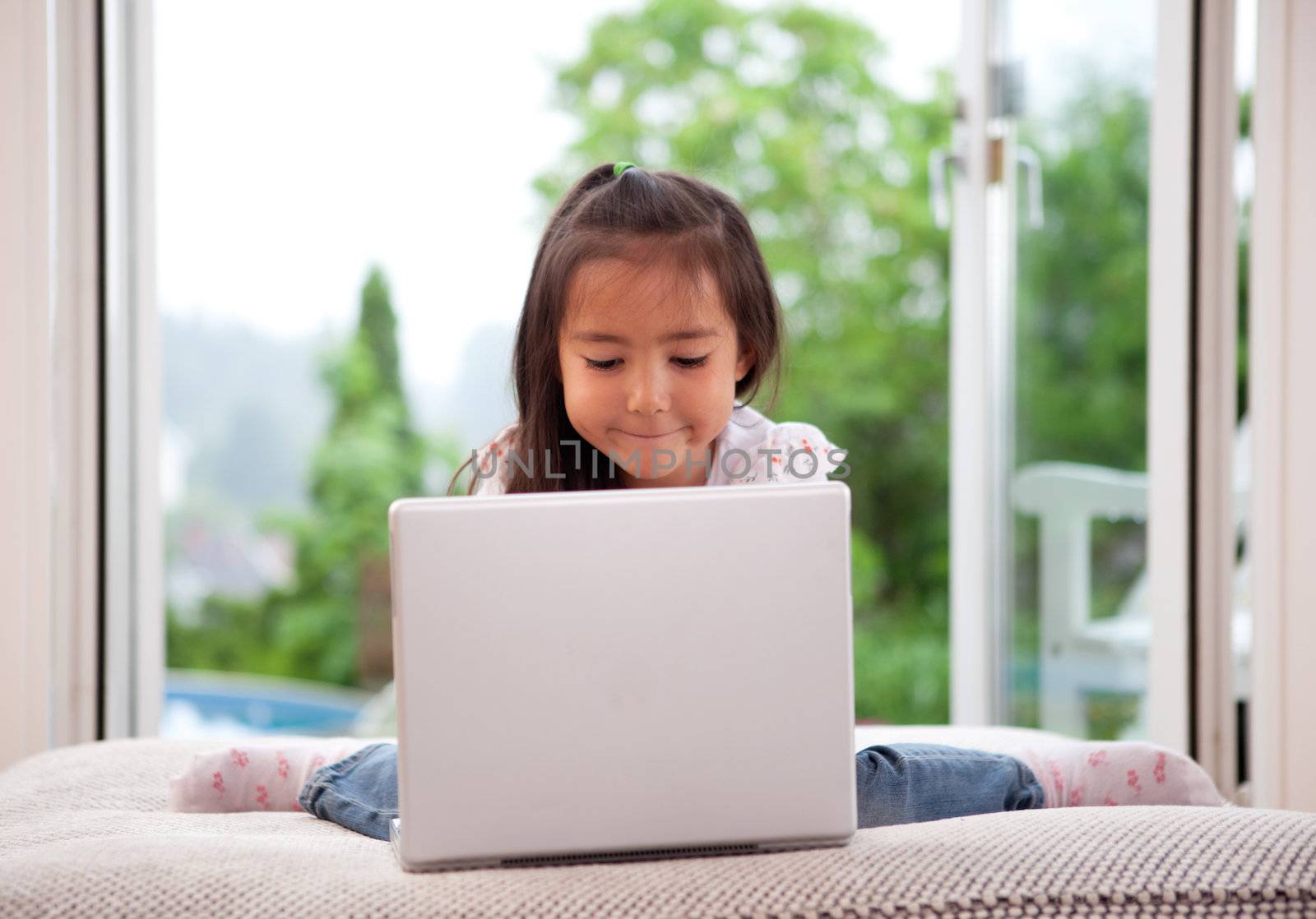 Young cute child using a computer in an indoor living room setting with large window