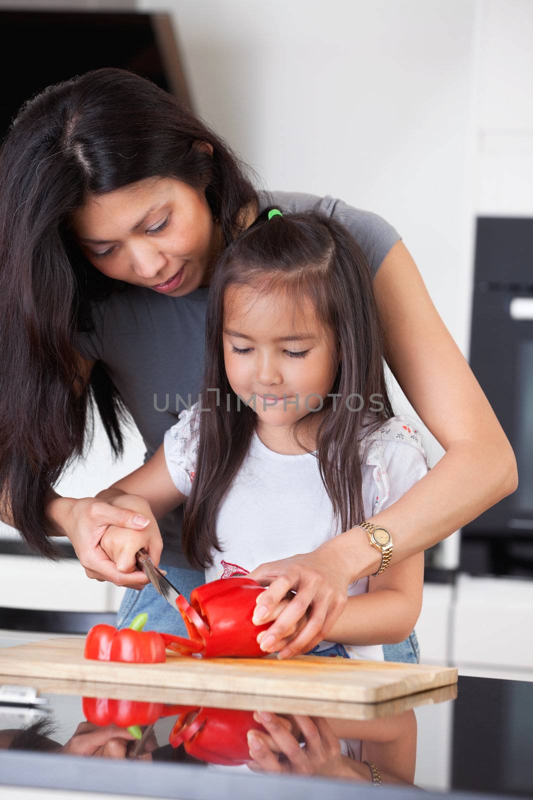 Little girl cutting pepper with the help of her mother