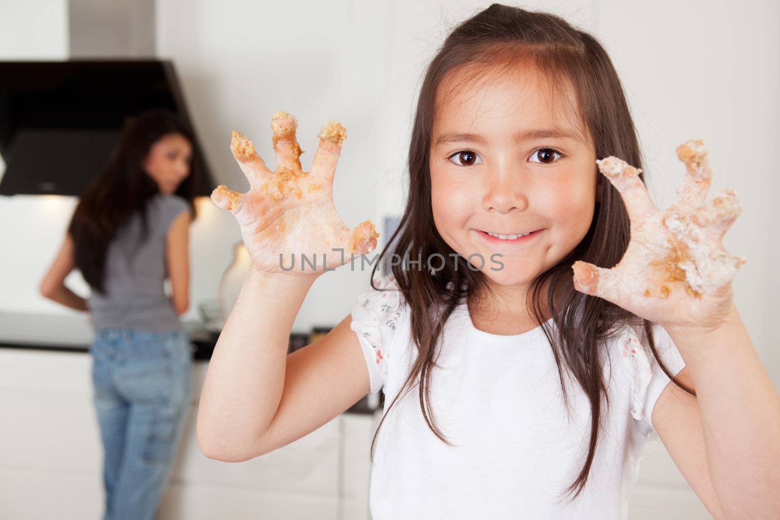 Mother and daughter in kitchen, child looking at camera with cookie dough on hands