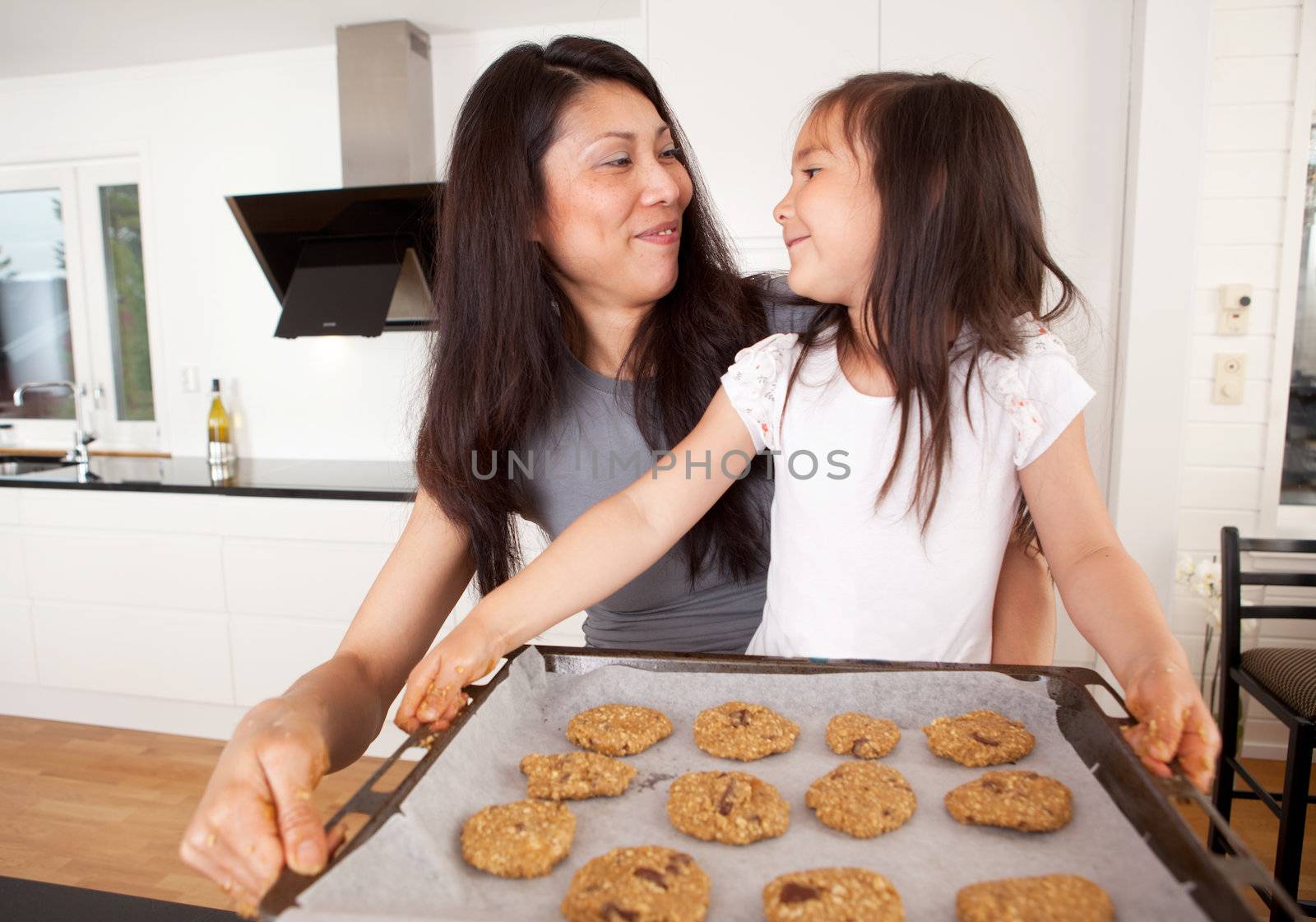 Mother and daughter baking cookies together, holding tray of raw cookie dough