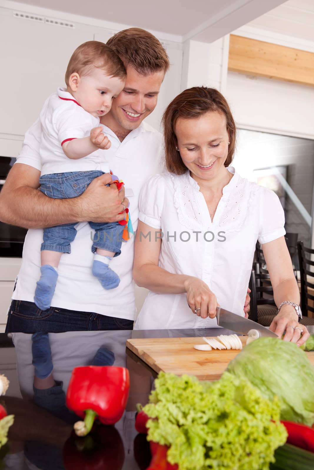 Happy family with mother, father and young toddler son in ktichen preparing food