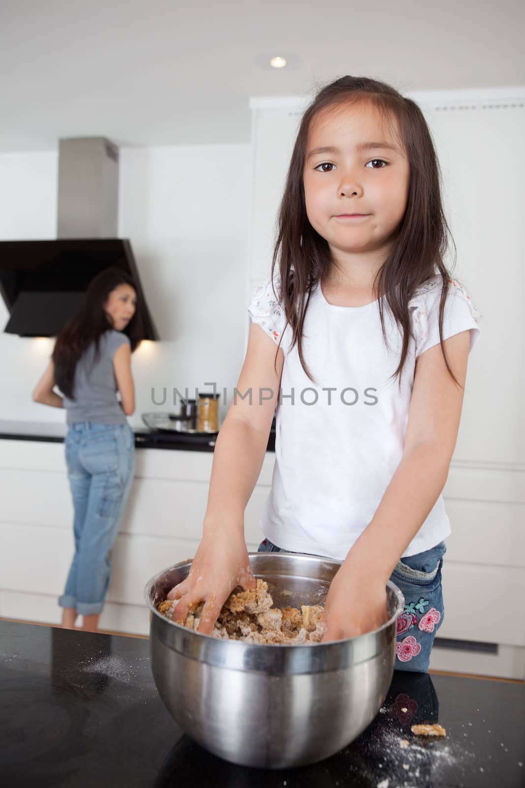 Girl mixing dough with mother in background by leaf
