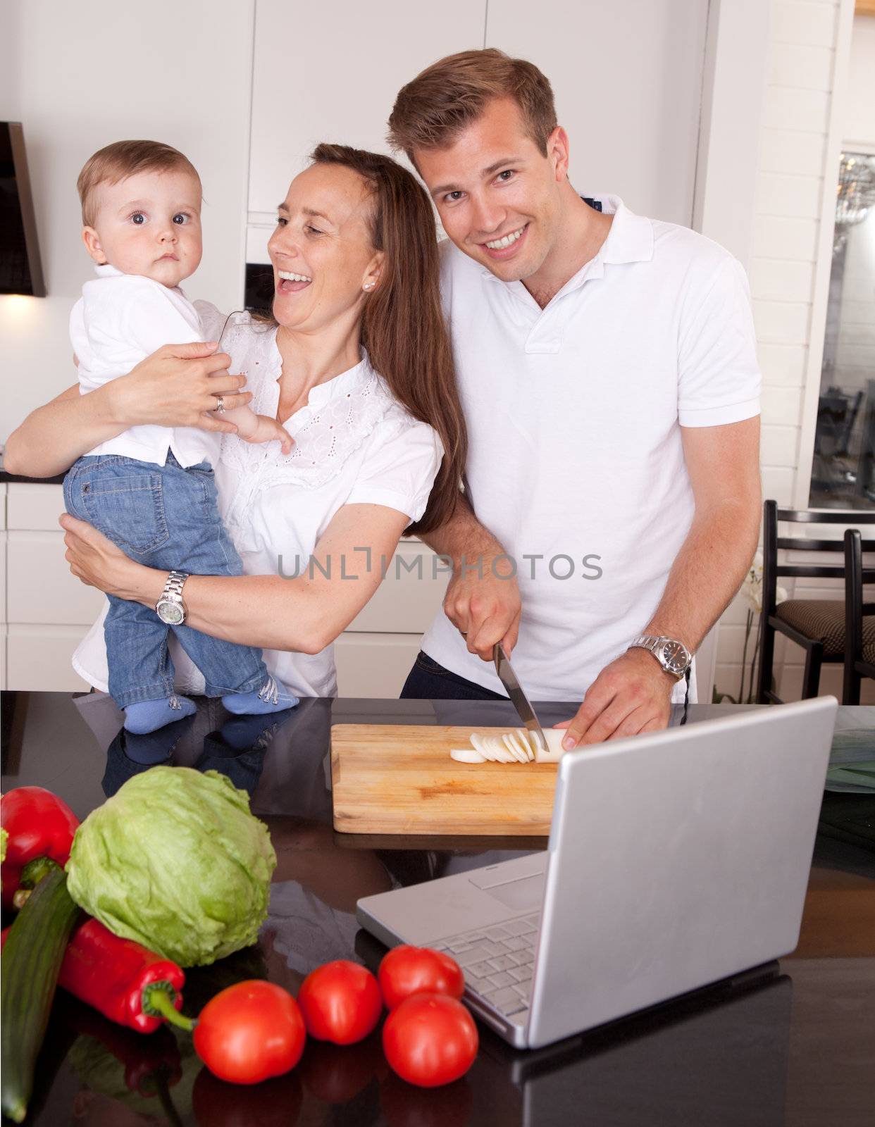 A happy mother and father with young toddler son,  having fun making food in the kitchen with online recipe