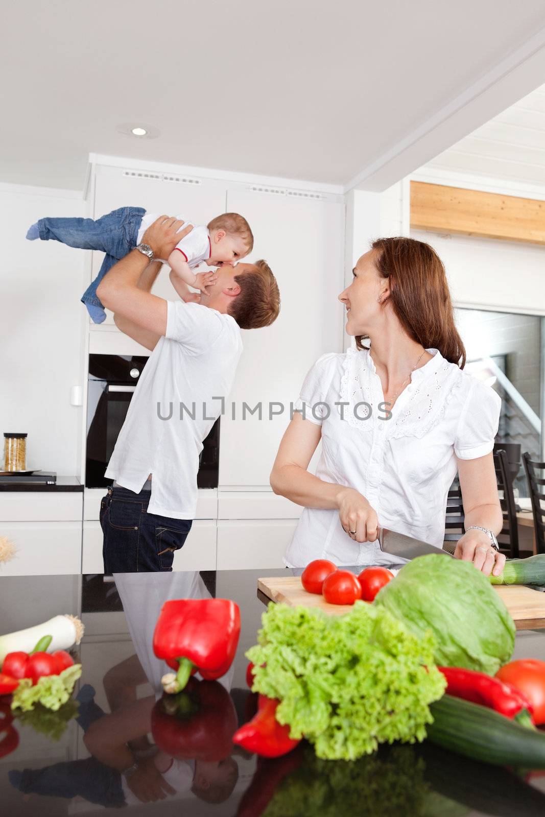 Father playing with child while mother cuts vegetables in kitchen