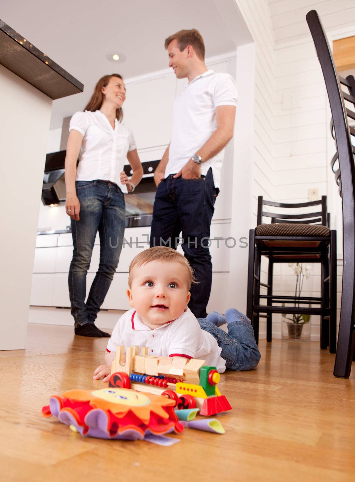 Baby Playing on Floor with Parents in Background by leaf
