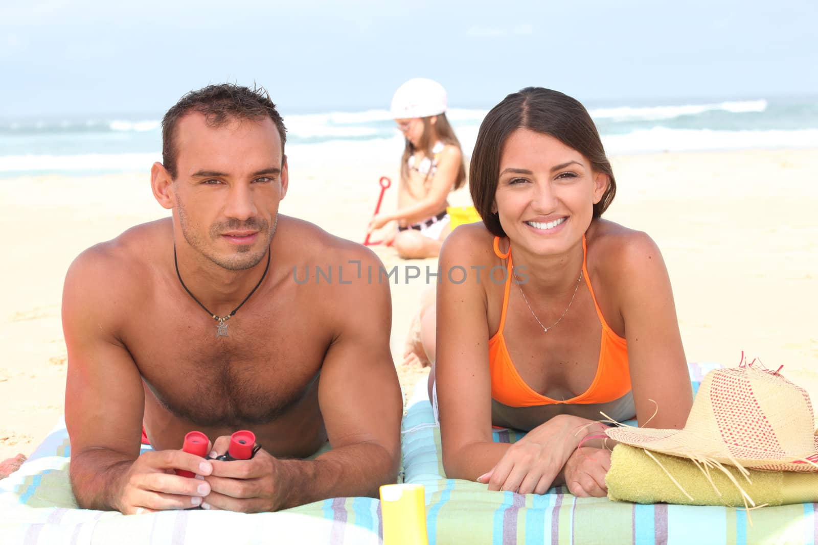 Parents sunbathing as their daughter plays in the sand behind them