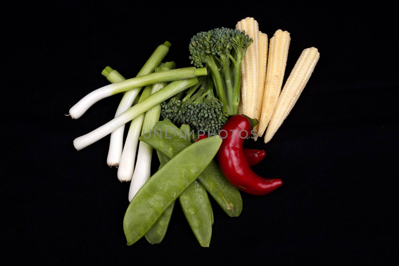 chilli, broccoli, baby leek, baby corn and mange tout on a black background