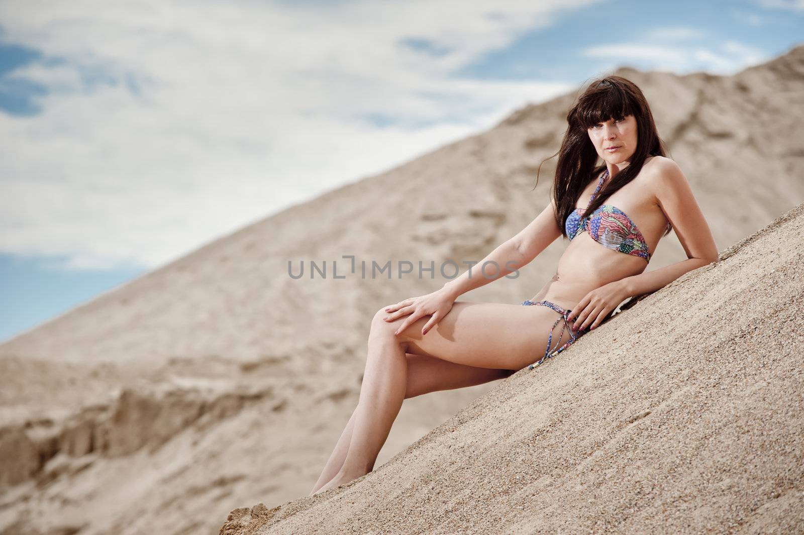 Young thin girl in a swimsuit posing on the sand in the sky.