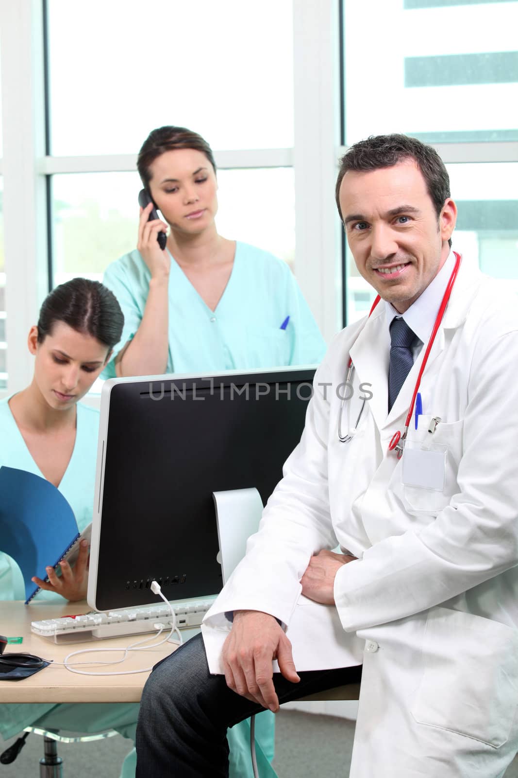 Doctor sitting with nurses at a computer by phovoir