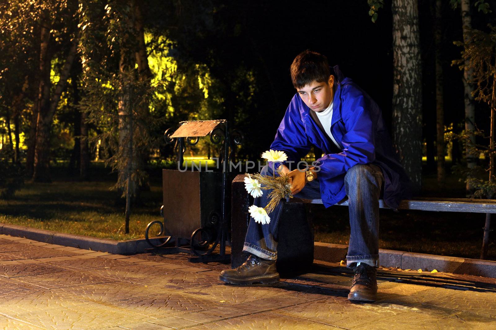 sad and lonely teenager with flowers sitting in the night park