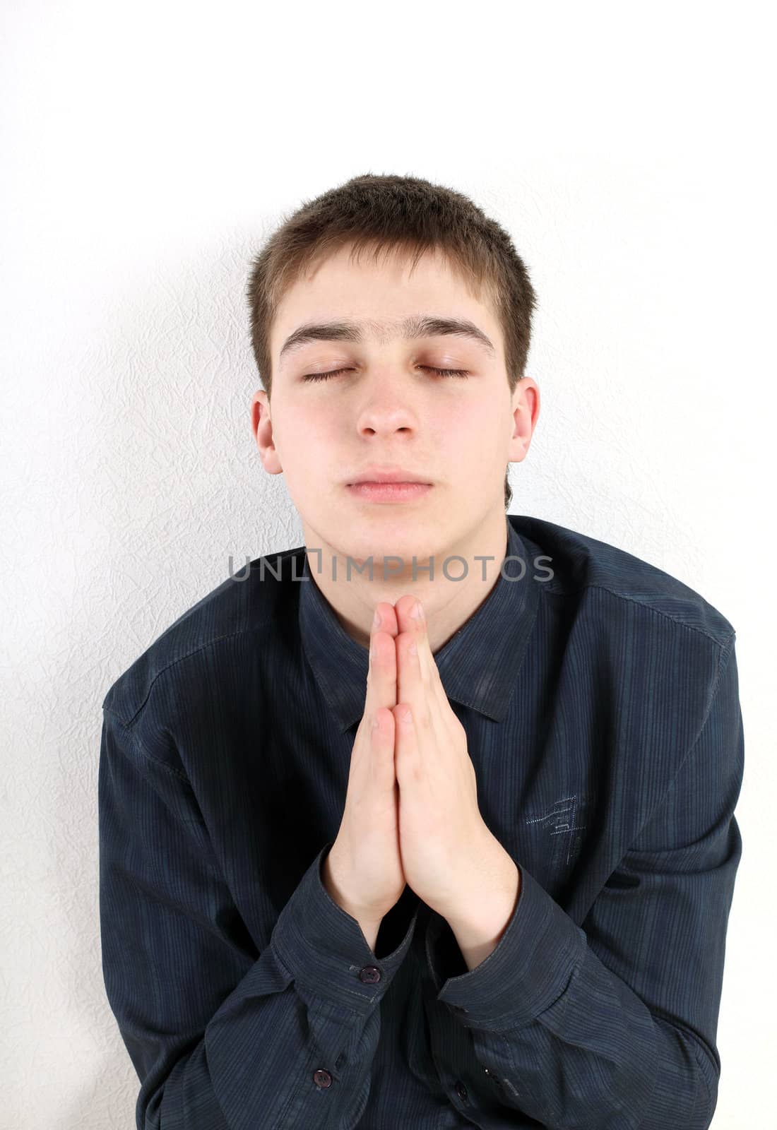 Teen prays against a white wall