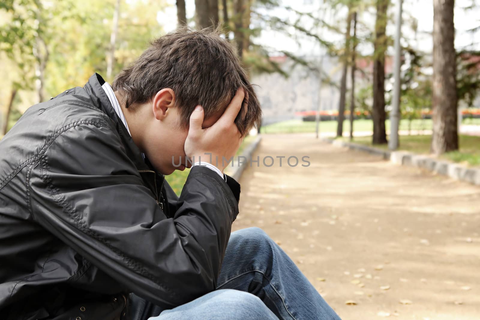 sad young man sitting in the autumn park