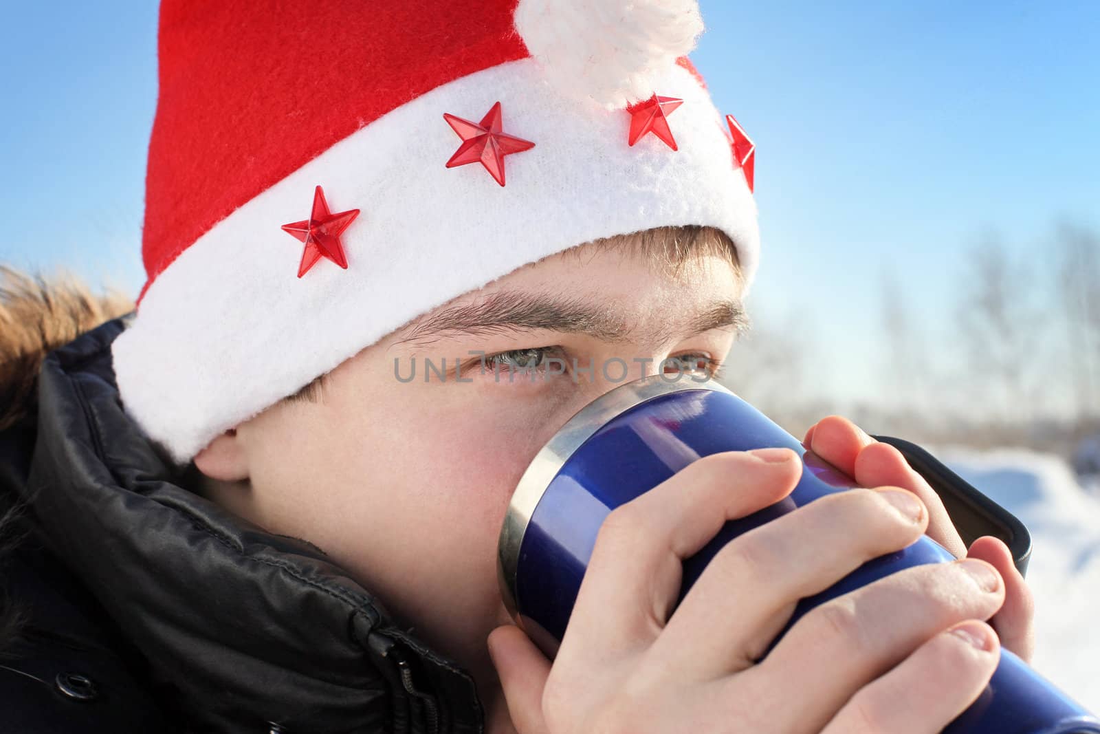 young man in santa's hat with travel mug in the winter