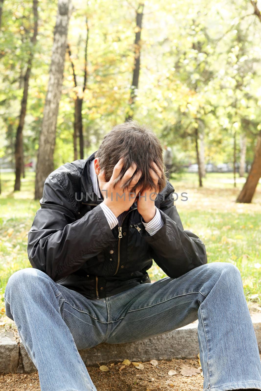 sad young man sitting in the autumn park