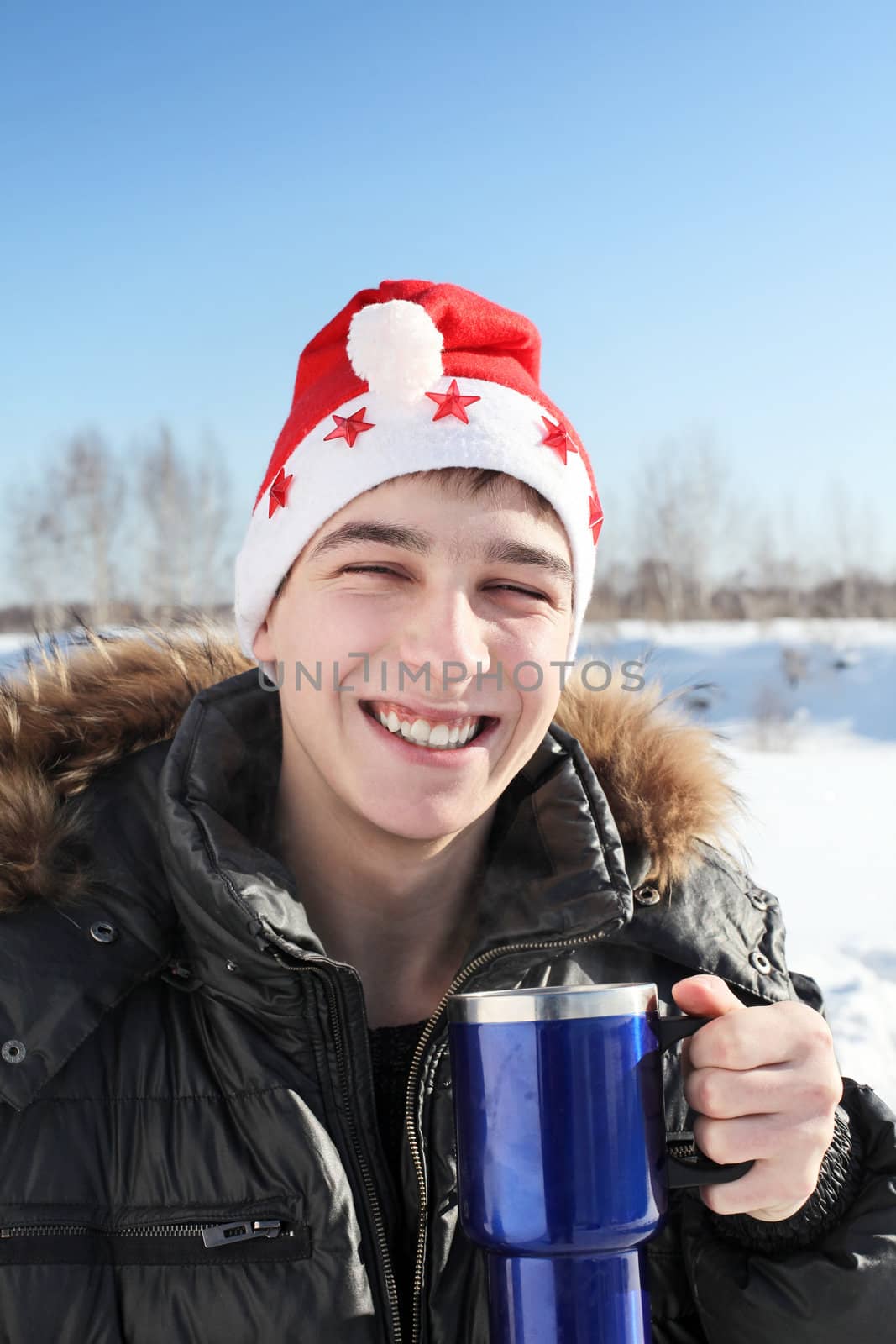 happy young man in santa's hat with travel mug in the winter