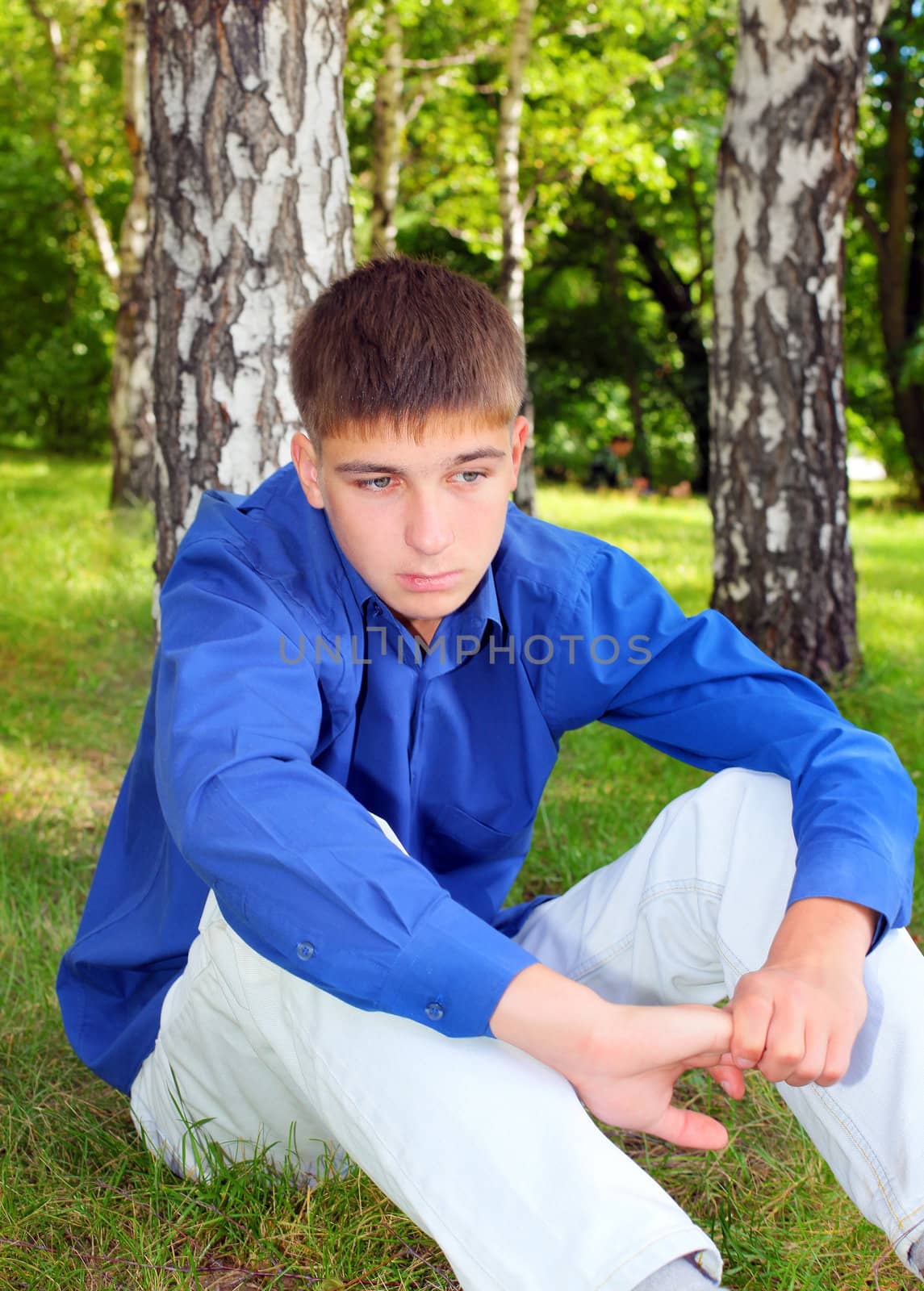 Sad Teenager sitting on the Grass in the Summer Park