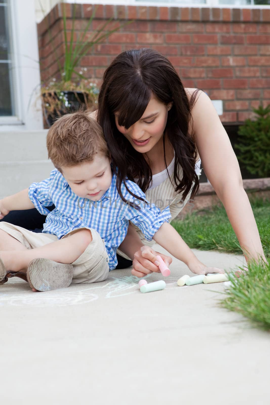 Young mother and son drawing on sidewalk with chalk