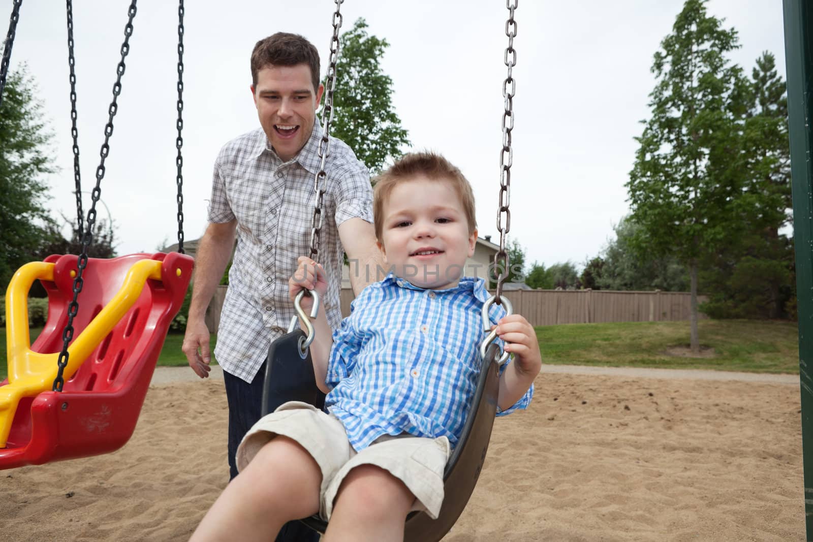 Happy father pushing boy on swing in playground