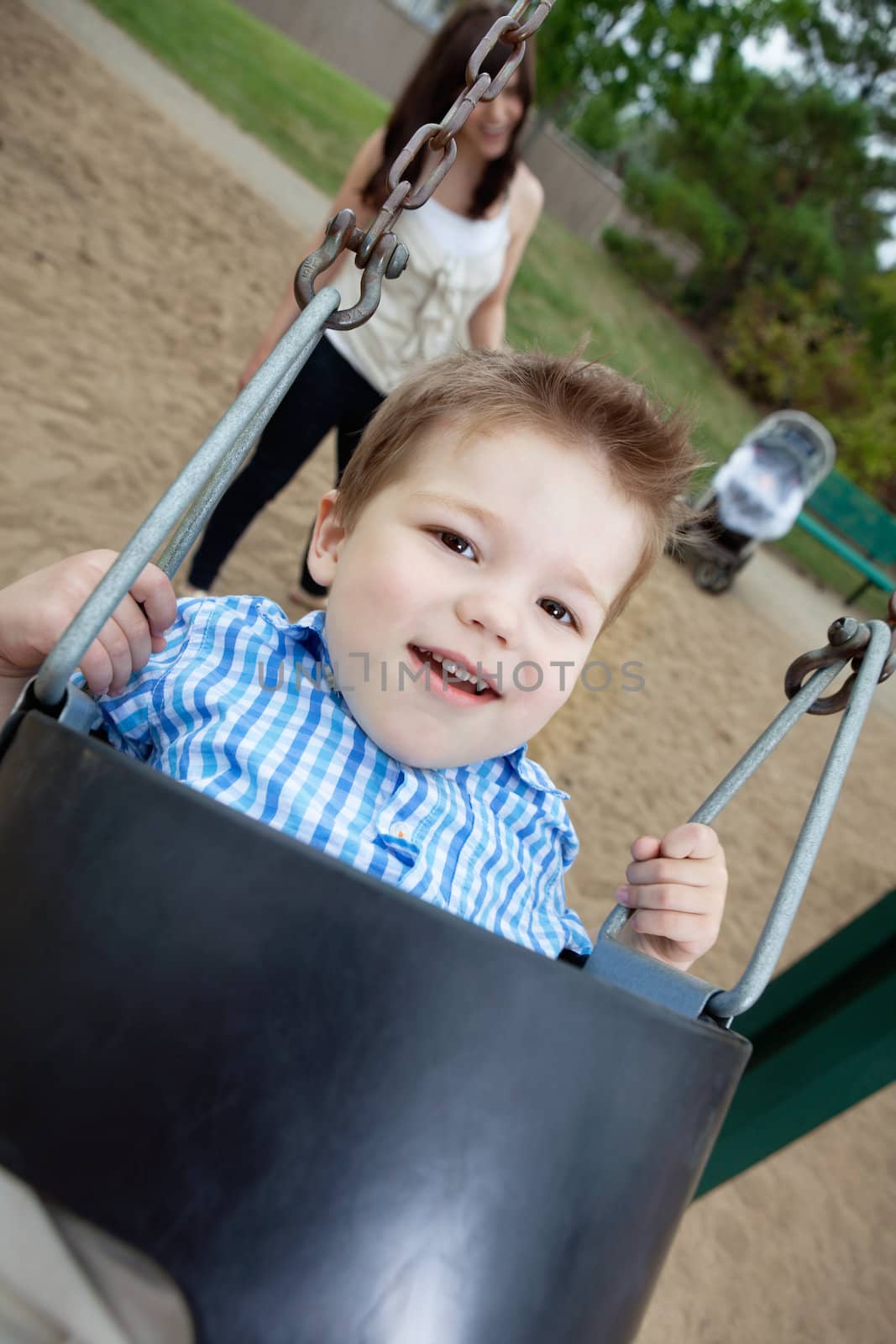 Close-up portrait of small boy swinging while mother standing in background