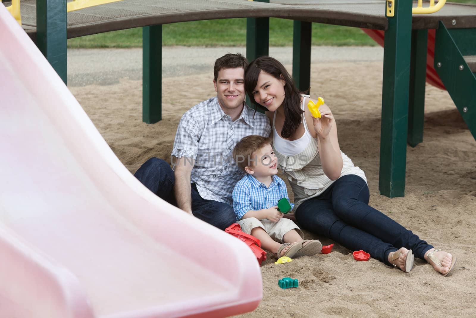 Portrait of happy couple sitting with their son in playground