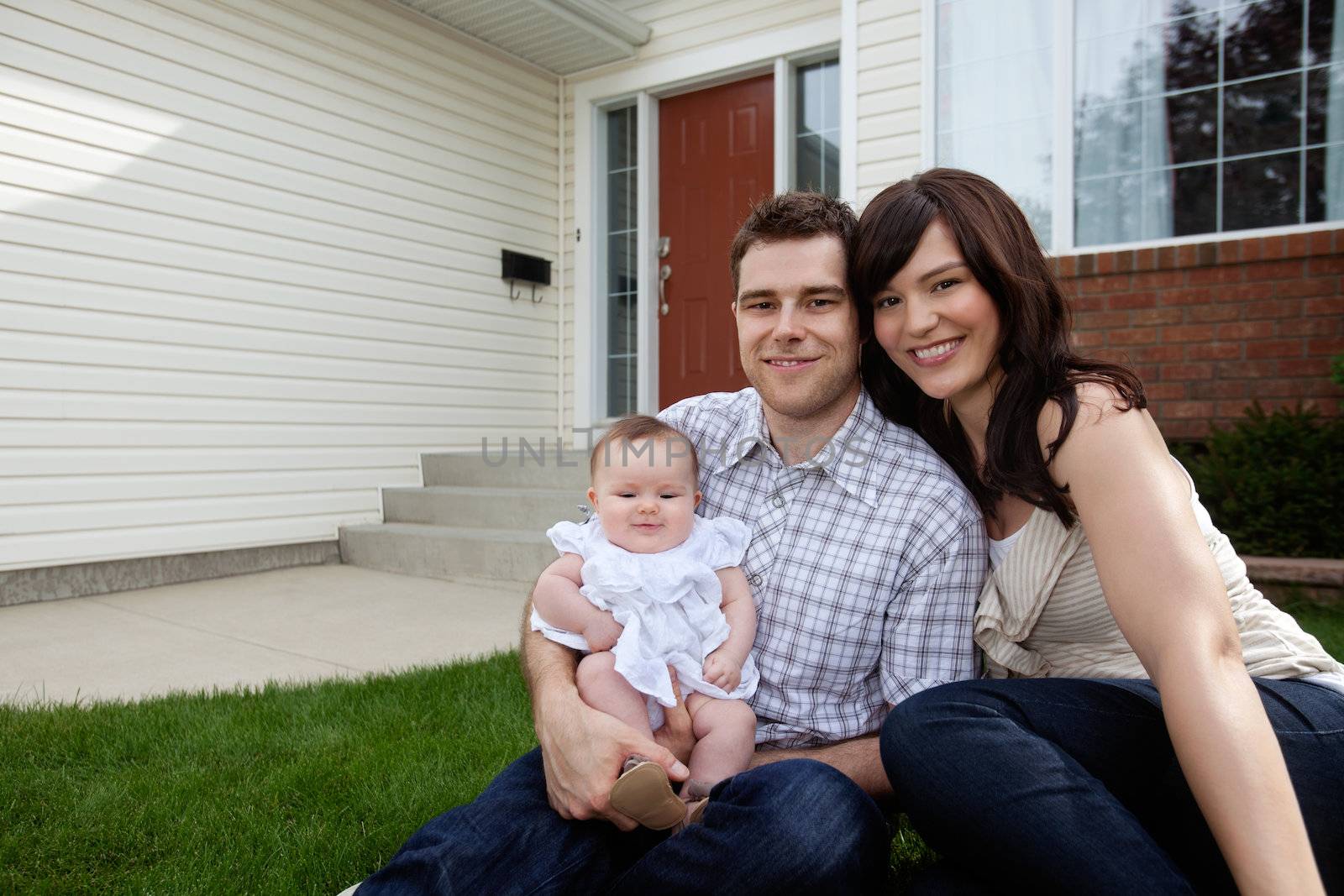 Portrait of couple with their adorable daughter sitting in front of house