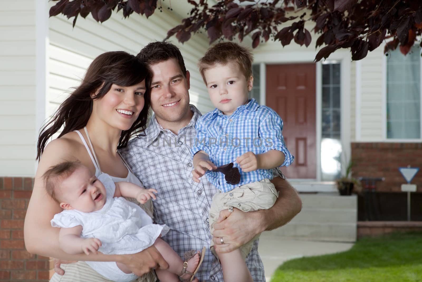 Portrait Of Sweet Family Standing In Front Of Their House.