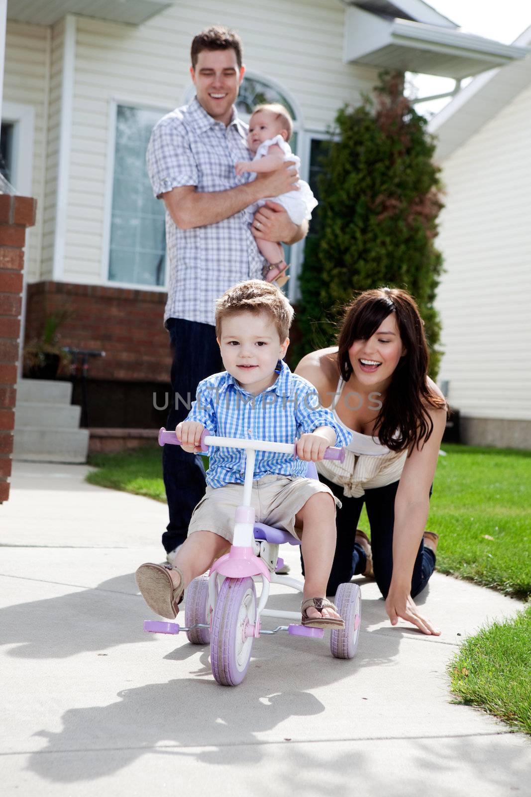 Young happy boy riding tricycle with family watching