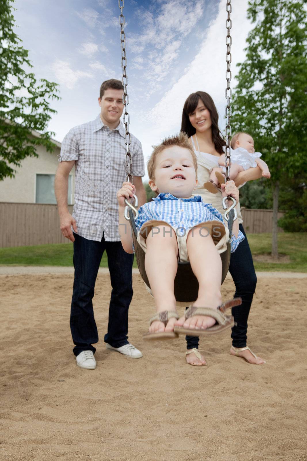 Father And Mother Pushing Boy On Swing by leaf